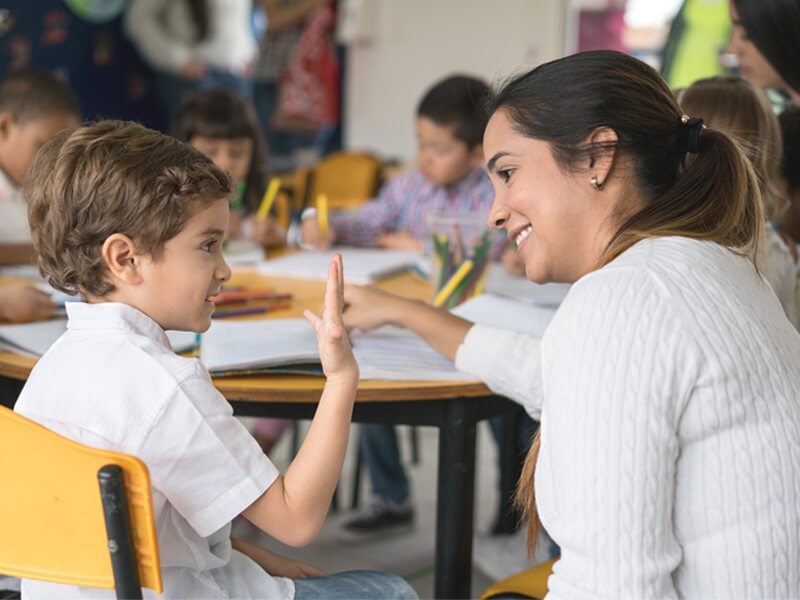 Una maestra ayudando a su estudiante, un niño en su escritorio