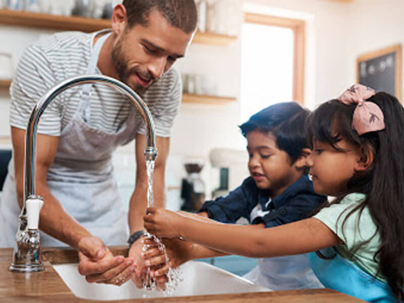 Un papa y sus hijos lavandose las manos